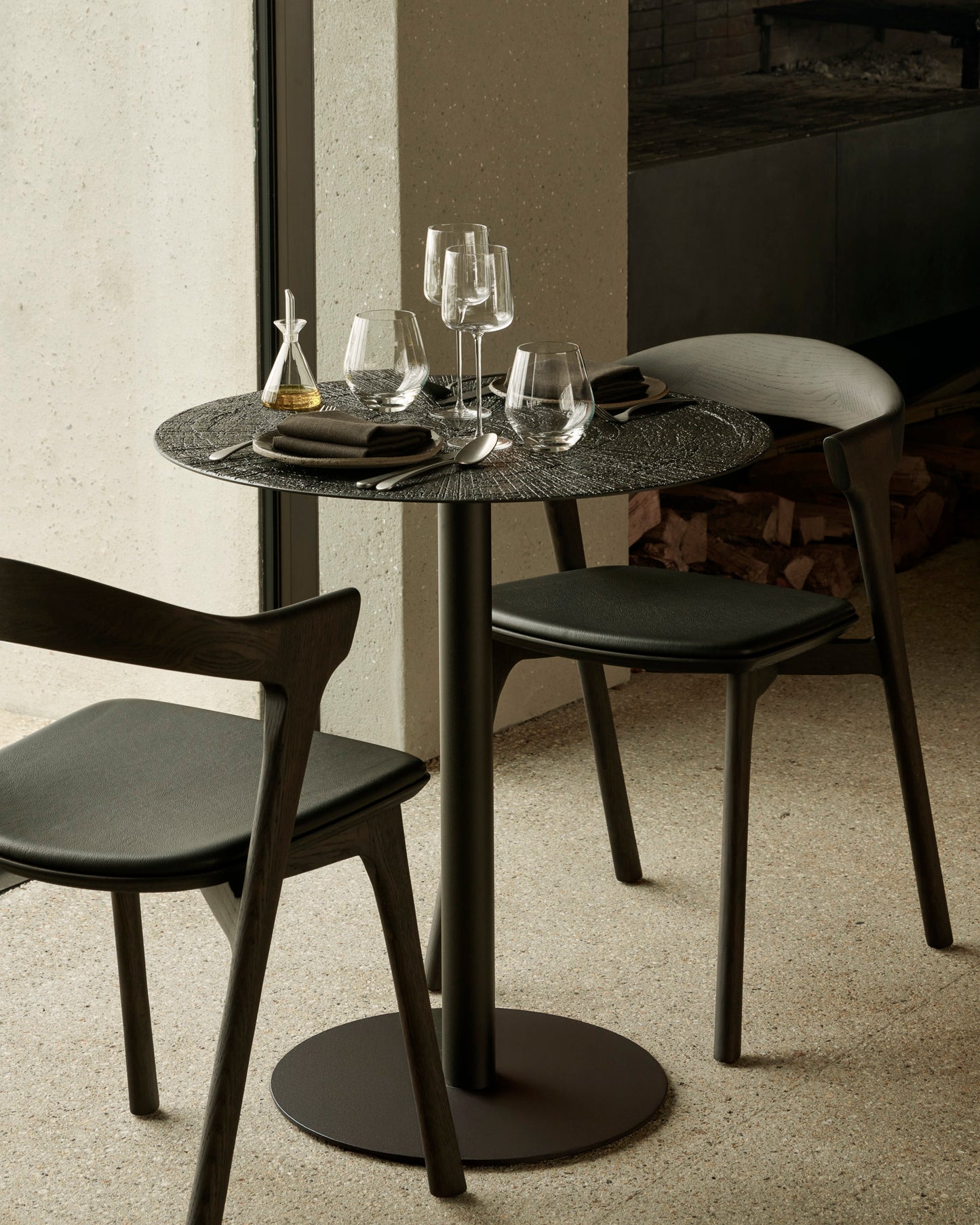 Round table with round top and base, surrounded by black chairs in a modern setting.